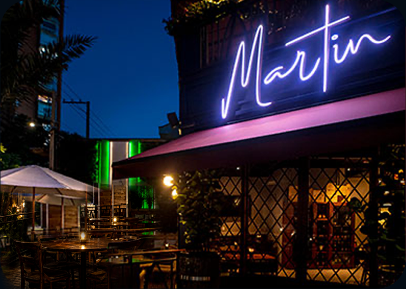 Fachada do Martin Bar à noite, com letreiro de neon